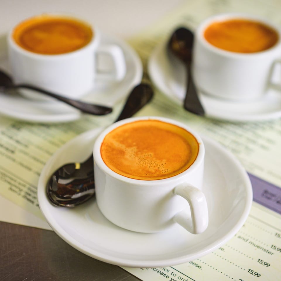 Three white cups of espresso with spoons on saucers, resting on a restaurant menu.