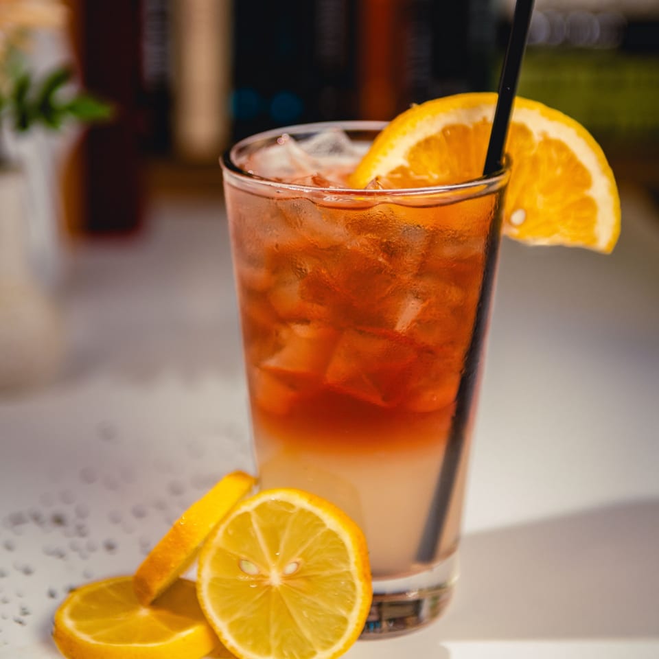 A refreshing iced tea with lemon slices and an orange wedge on a white surface.