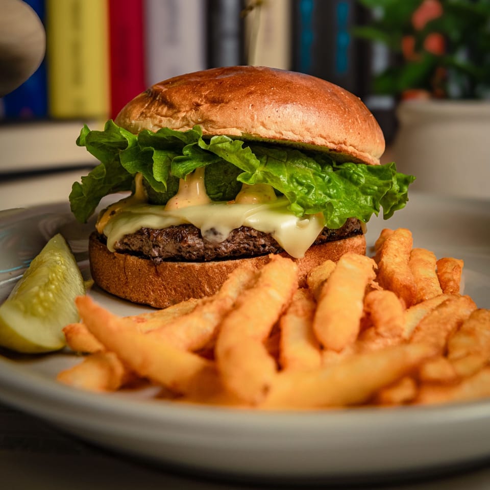 A cheeseburger with lettuce and special sauce, served with golden french fries and a pickle spear.