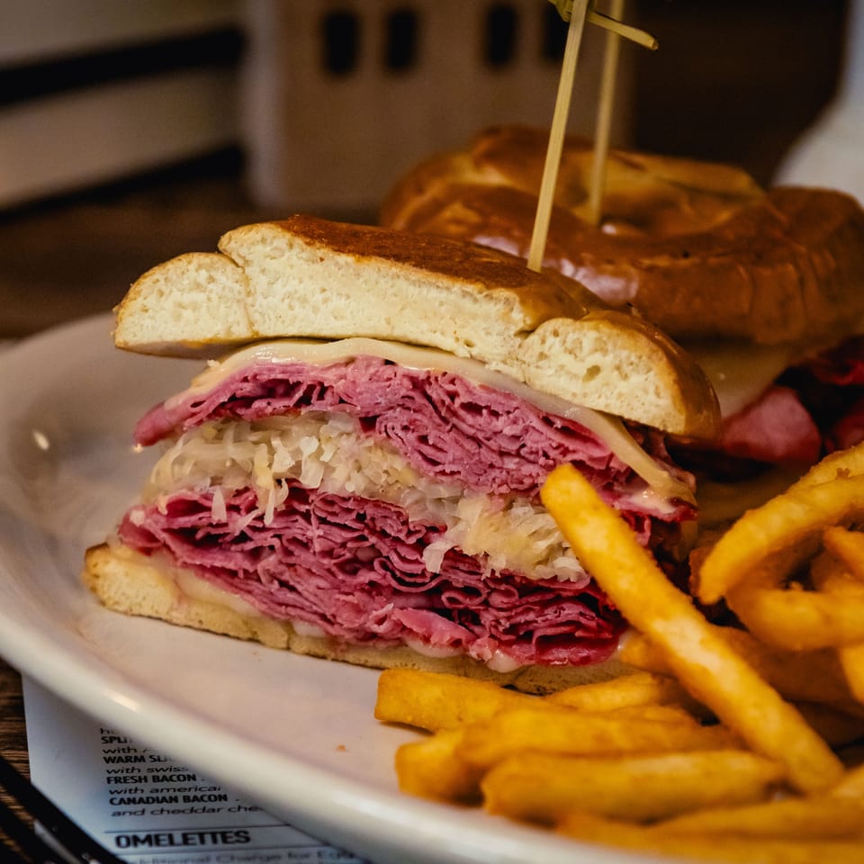 A close-up of a reuben sandwich with corned beef, sauerkraut, and cheese, served with fries.