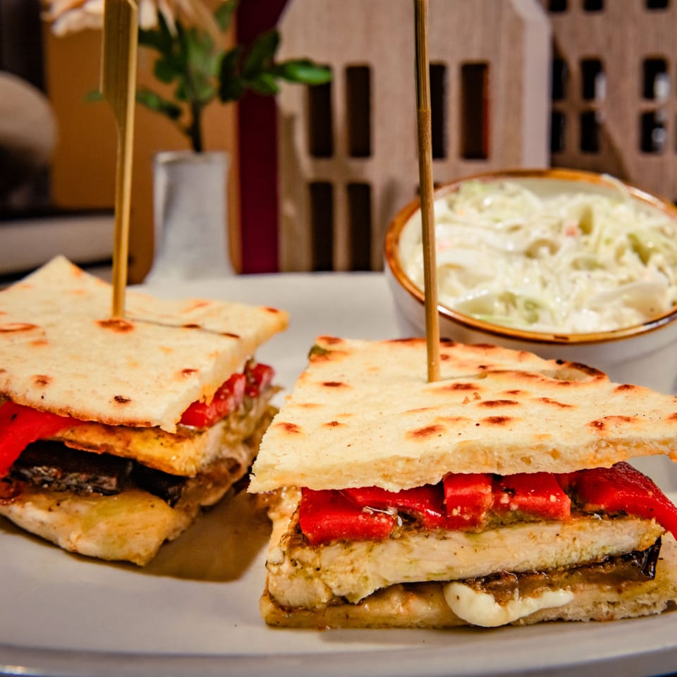 Two flatbread sandwiches with chicken, red peppers, and cheese, served with coleslaw.