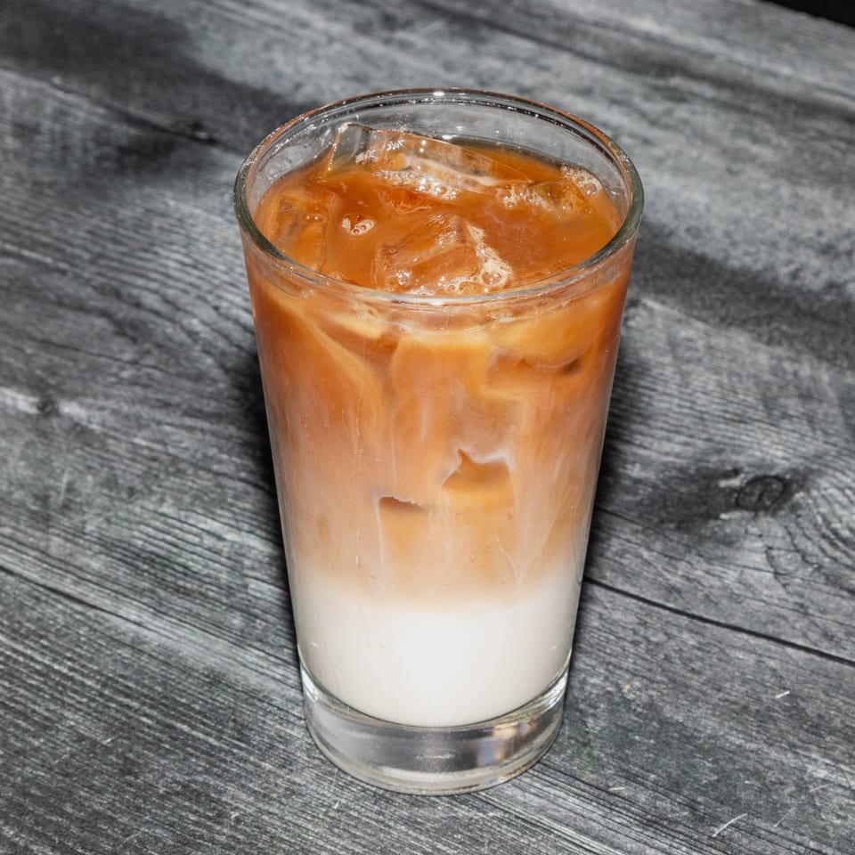 Iced Thai tea with milk and ice in a clear glass on a dark wooden table.