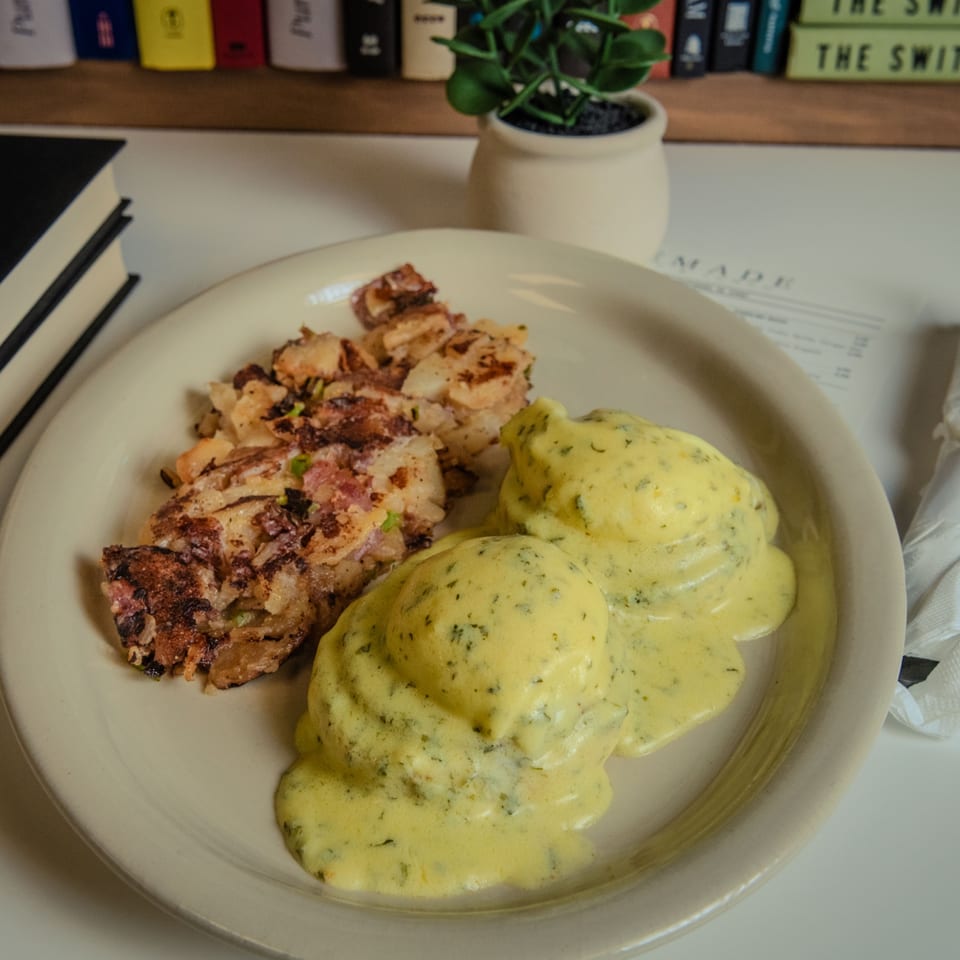 Eggs Benedict with hollandaise sauce and a side of crispy hash browns on a white plate.